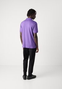 Lila polo skjorta med krage, korta ärmar, kombinerad med svarta byxor och svarta sneakers. Synlig textur och passformsdetaljer är inte specificerade.