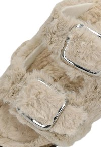 Wollen beige pantoffels met twee verstelbare zilverkleurige gespen, zachte textuur en een gevoerde binnenzool.