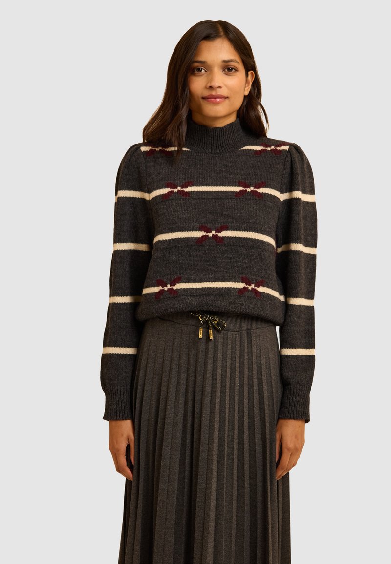 Maglione grigio a maglia con strisce bianche e bordeaux, colletto alto e maniche a sbuffo, abbinato a una gonna plissettata grigia con vita regolabile.