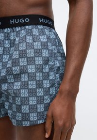 Μπόξερ σορτς με γεωμετρικό μοτίβο σε μπλε και γκρι αποχρώσεις και λογότυπο "HUGO" στη μέση. Υφασμάτινη υφή με άνετη, χαλαρή εφαρμογή.