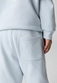 Svetlo modrý sveter s ryhovanou textúrou, obsahujúci malú bočnú kapsu a logo "ALLSAINTS" v bielej farbe. Jednoduchý, uvoľnený strih.