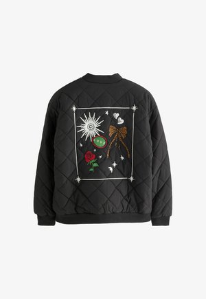 Černá prošívaná bunda se vzorem výšivky na zádech – slunce, mašle s leopardím vzorem, červená růže, dvě srdce, hvězdy a zelená nášivka „LOVE“ uvnitř bílého obrysu.