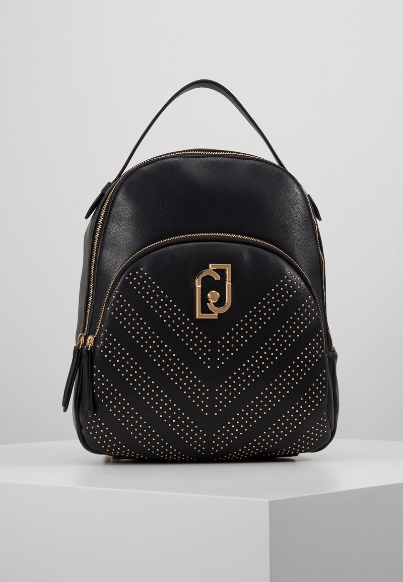 Mochila de cuero negro con un patrón de chevron de tachuelas doradas, herrajes dorados, un asa en la parte superior y un compartimento principal con cremallera.