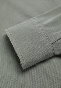 Mânecuță din stofă texturată gri, cu un finisaj curat și cusături vizibile. Stofa are un model cu nervuri, subliniind durabilitatea și structura.