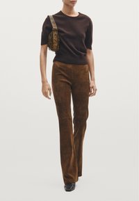 Brown fitted sweater, brown suede flared pants, and a patterned shoulder bag. The outfit features a smooth texture and neutral tones.