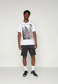 Camiseta de algodón blanca con un estampado gráfico de Spiderman, combinada con pantalones cortos negros y zapatillas deportivas negras con acentos blancos.