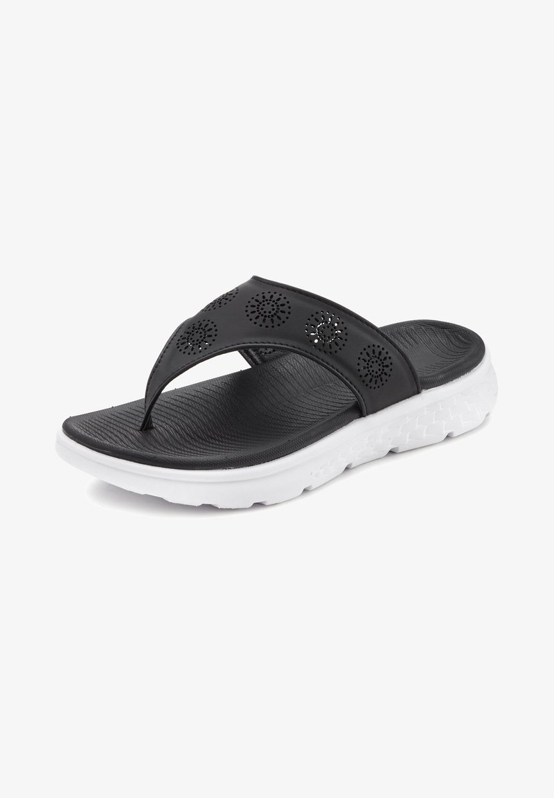 Mustan perforatsioonide ja tekstuuriga jalgealusega plätud, millel on valge sünteetilisest materjalist geomeetrilise mustriga põhi.