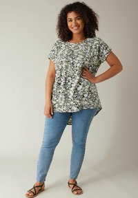Bluse med blomsterdesign og korte ærmer med sorte, hvide og grønne accenter; afslappet pasform; kombineret med lyseblå skinny jeans og sorte sandaler.