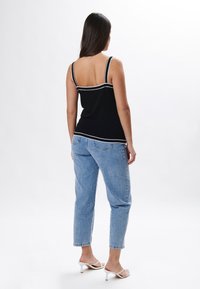 Top de tirantes negro con detalle de rayas blancas, con un diseño ajustado. Combinado con jeans de un azul claro y sandalias de tacón blancas.