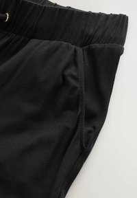 Pantalones cortos de algodón negros con una cinturilla elástica, con detalles de costura y un bolsillo lateral. Textura suave, diseño casual.