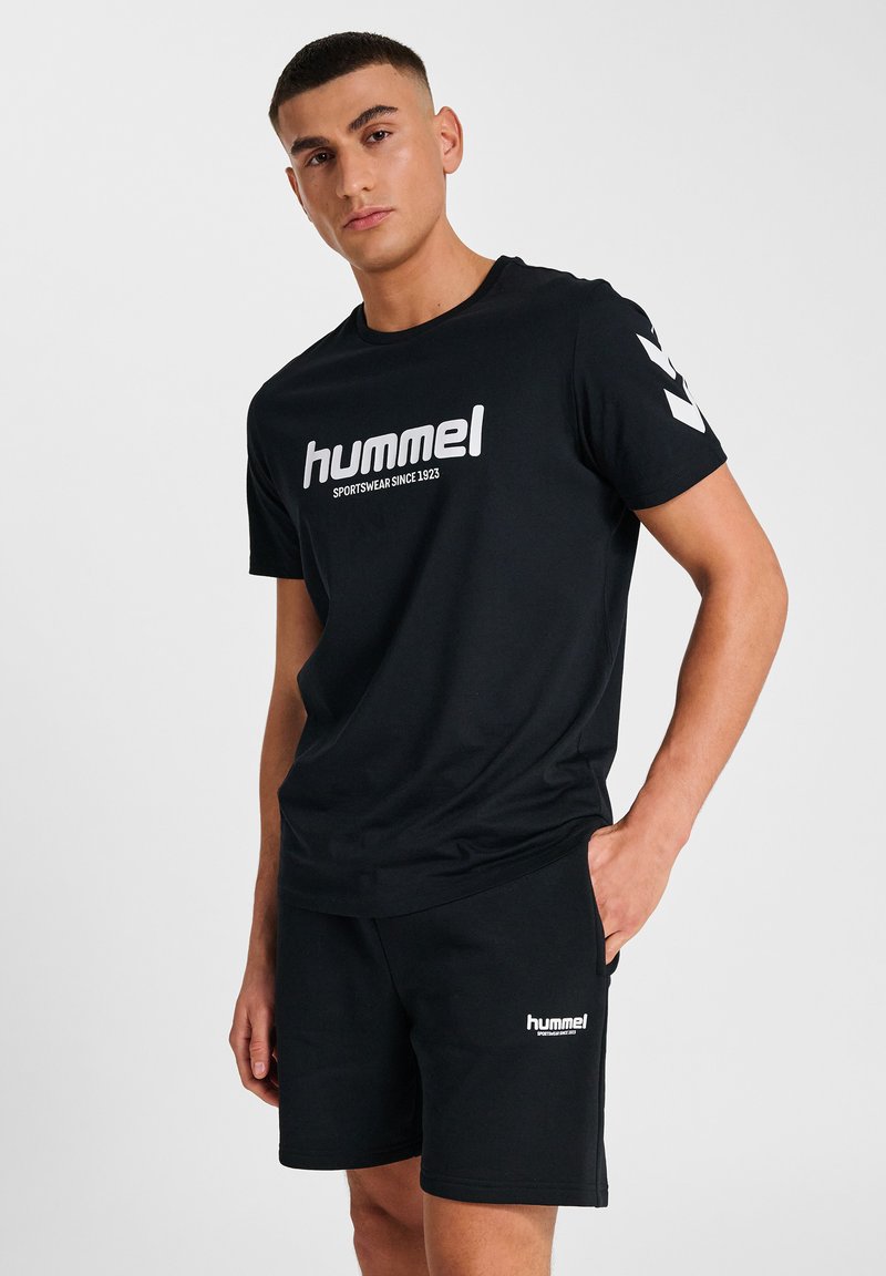 Schwarzes Sport-T-Shirt mit Rundhalsausschnitt, mit einem auffälligen weißen Logo und Text. Dazu eine passende schwarze Shorts mit Logodetails.