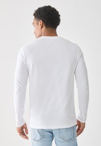 Langermet hvit T-skjorte i mykt stoff, med et enkelt rundhalset design. Synlig søm langs skjortefaldet og mansjettene. Ledig passform.