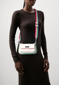 Borsa a tracolla in pelle testurizzata color crema con dettagli verdi e rosa. Presenta una tracolla regolabile a strisce arcobaleno e finiture in argento.