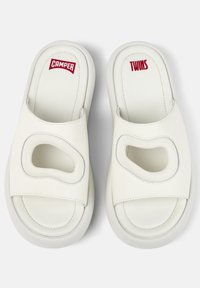 Vita slidessandaler med en slät läderöverdel, med utskärningar, grå sömmar och kontrasterande röda varumärkeslogotyper "CAMPER" och "TWINS."