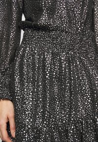 Robe en tissu noir avec un motif d'étoiles argentées. Manches longues, taille smockée et jupe à volants. Aspect texturé.