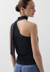 Zwarte mouwloze top met een hoge hals die aan de achterkant vastgebonden wordt, gemaakt van zachte stof. Draagt bij hoge taille blauwe denim jeans.