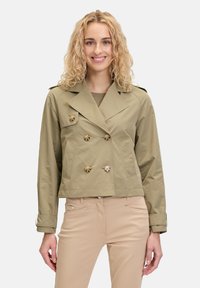 Kaki cropped trenchcoat met dubbelbreasted sluiting, grote knopen en zijzakken. Heeft een klassieke kraag en verstelbare mouwmanchetten.