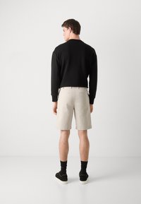 Black sweatshirt, beige shorts, and black sneakers with white soles. The fabric is smooth, and the shorts have a relaxed fit with pockets.