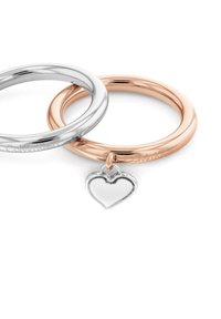 Dos anillos entrelazados, uno de plata y otro de oro rosado, con un charm en forma de corazón de plata. Ambos anillos presentan una superficie lisa y pulida.