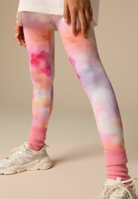 Leggings colorati e leggeri presentano un motivo tie-dye in tonalità pastello di rosa, viola e blu, con un orlo testurizzato e calzini rosa abbinati.