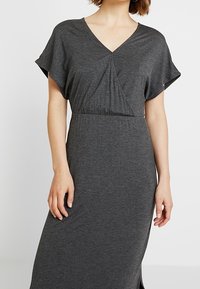 Graues Maxikleid aus weichem Stoff; verfügt über einen V-Ausschnitt, kurze Flügelärmel und eine geraffte Taille für einen lässigen Sitz. Keine sichtbaren Muster oder Beschläge.