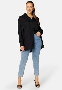 Camicia nera con bottoni, maniche lunghe, vestibilità comoda, abbinata a jeans in denim blu chiaro e tacchi aperti neri.