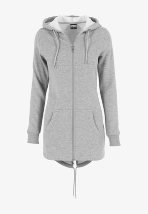 Harmaa zip-up huppari, jossa on suuri huppu, nyörit, etutaskut ja kaareva helma. Valmistettu pehmeästä ja tekstuurista kankaasta, jossa on kontrastivärinen vuori.