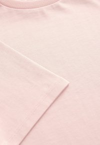 Helles rosa T-Shirt mit geripptem Halsausschnitt. Glatte Textur, kurze Ärmel und sichtbare Nähte entlang der Kanten. Einfaches, ungeschmücktes Design.