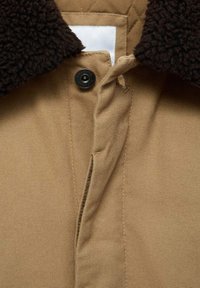 Beżowa kurtka koszulowa z brązowym kołnierzem z Sherpa, zapięciem na zatrzaski i pikowaną podszewką; tkanina o fakturze z widocznym przeszyciem.