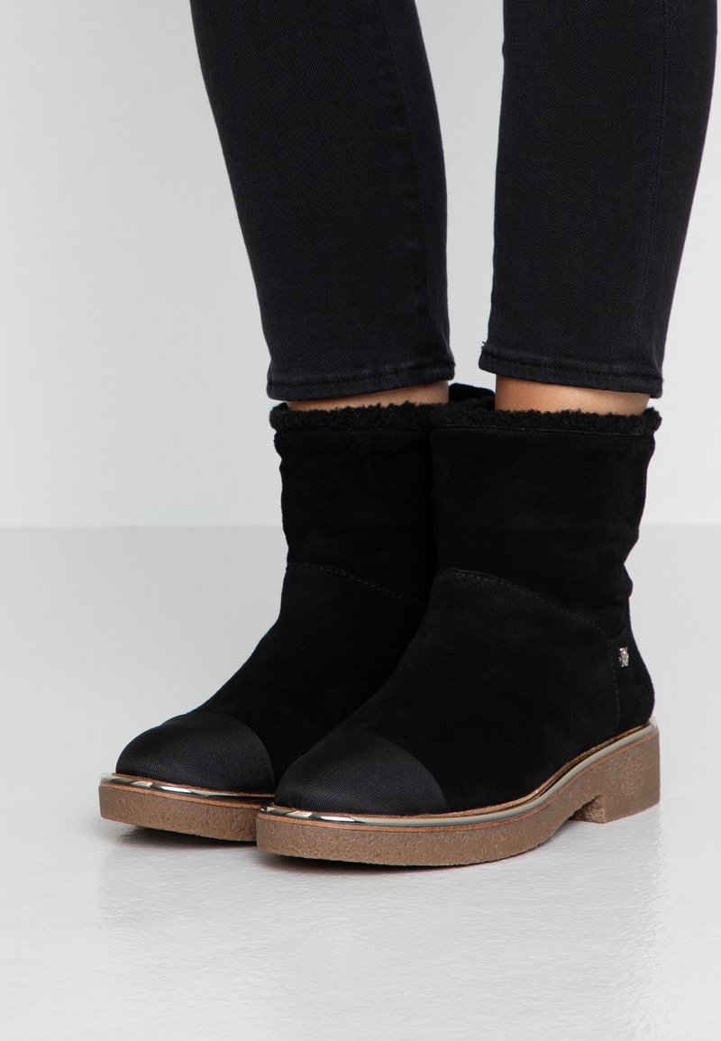 Svarta mocka ankelskor med bruna gummisulor, runda förstärkta tår och fluffig foder, som bärs med svarta tajta byxor.