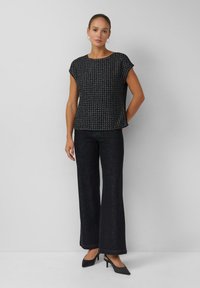 Czarny teksturowany sweter z okrągłym dekoltem i krótkimi rękawami, zestawiony z rozszerzanymi ciemnymi dżinsami i czarnymi szpilkami z noskiem w szpic.