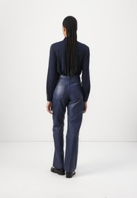 Blouse navy à manches longues associé à un pantalon en cuir bleu foncé taille haute avec une texture lisse et un design de poche arrière unique.