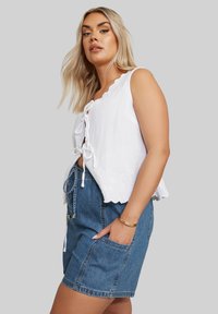 Top blanco de lino con dobladillo festoneado y cierre con cordones, combinado con shorts de mezclilla azul que cuentan con bolsillos laterales y cordón de ajuste.