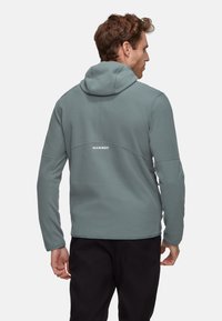 Grauer Fleece-Hoodie mit figurbetontem Design, ausgestattet mit einer Kapuze und einem sichtbaren Markenlogo auf der Rückseite. Glatte Textur und schlichter Stil.