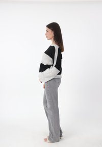 Schwarzer und grauer gestrickter Pullover mit weiten Ärmeln, rundem Halsausschnitt und horizontalen Streifen, kombiniert mit hellgrauen geraden Jeans.