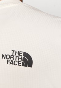 Bílá krátká košile s texturou připomínající mřížku a černým logem "The North Face" na horní části zad.
