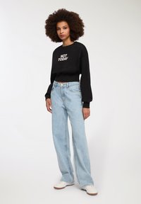 Felpa nera corta con "NOT TODAY" in testo bianco, abbinata a jeans a gamba larga blu chiaro e sneakers bianche.