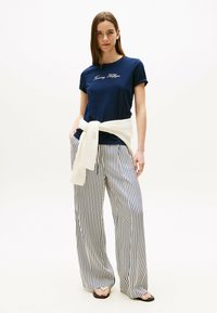 Marineblå bomuldst-shirt med "Tommy Hilfiger" broderet, parret med hvide og marineblå stribede brede bukser, med en knyttet striktrøje om taljen.