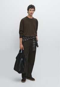 Dunkelbraunes Langarmhemd kombiniert mit passenden Hosen. Ein grau gestreifter Pullover, um die Taille gebunden, und eine schwarze Wildleder-Shopper-Tasche.