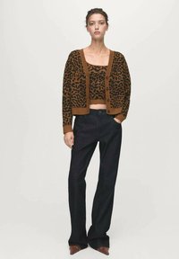 Cardigan s leopardím vzorom a hnedým lemom, gombík na prednej strane, nosený cez zodpovedajúci crop top; skombinovaný s tmavými širokými nohavicami a špicatými topánkami.