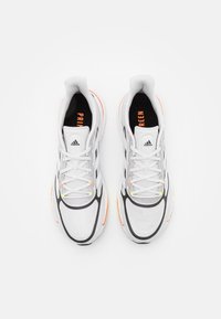Scarpe sportive bianche con parte superiore in mesh strutturato, dettagli neri, accenti arancioni brillanti e giallo neon, e un design con suola ammortizzata.