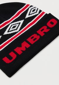 Čierna pletená čiapka s červeným textom "UMBRO" na leme a bielymi a červenými pruhmi s diamantovým vzorom nad ňou.
