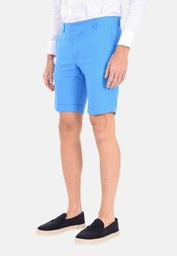 Bermuda blu tailorati con fronte piatto e risvolti, realizzati in tessuto leggero. Indossati con espadrillas blu scuro.