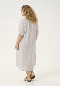 Abito di cotone a righe con maniche corte, lunghezza al ginocchio, caratterizzato da righe verticali in beige e marrone chiaro, orlo arrotondato e texture morbida.