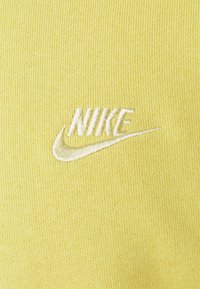 Gul stickad tyg har en broderad vit "Nike"-logotyp med en swoosh, vilket skapar en texturerad kontrast mot den släta bakgrunden.
