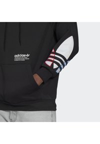 Felpa nera Adidas con cappuccio e coulisse, dotata di tasca frontale e accenti colorati sulle maniche: strisce rosse e blu su pannelli bianchi.