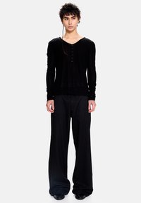 Haut noir ajusté à manches longues, col en V avec boutons sur le devant, associé à un pantalon large texturé noir. Tissu lisse et design minimaliste.