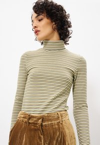 Gestreepte lange mouwen turtleneck in gedempt groen en roomkleur met donkergroene lijnen; zachte stof; aansluitend ontwerp. Gecombineerd met bruine fluwelen broek.