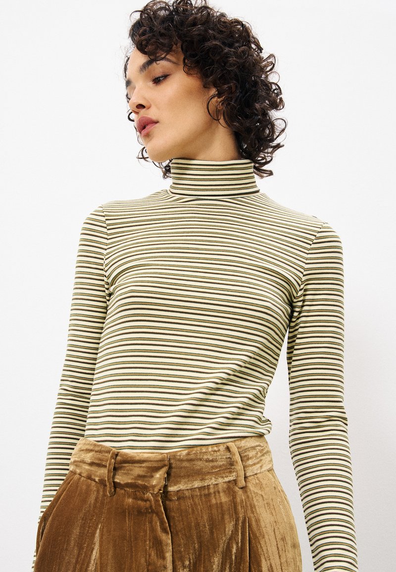 Gestreepte lange mouwen turtleneck in gedempt groen en roomkleur met donkergroene lijnen; zachte stof; aansluitend ontwerp. Gecombineerd met bruine fluwelen broek.