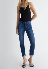 Bodysuit negro de canalé con detalle 'JUJO', combinado con vaqueros azul oscuro con puños enrollados y sandalias de tacón plateadas. Diseños simples pero definidos.
